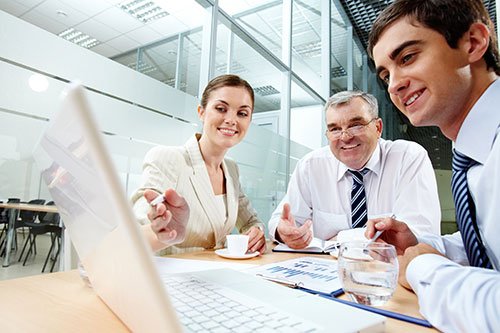 Three people working on a laptop in an office developing a marketing strategy